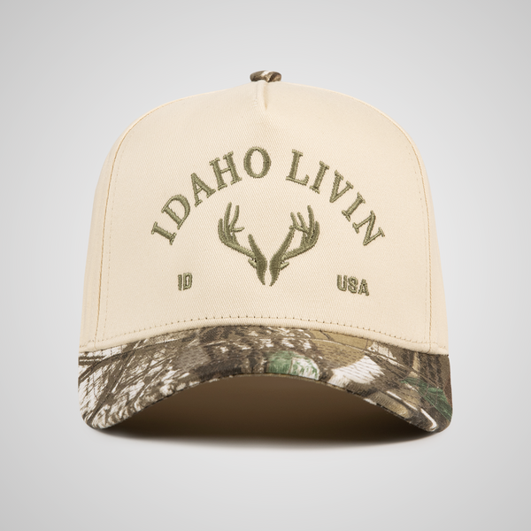 Beige and camouflage cap with 'Idaho Livin' and elk antler design on a gray background